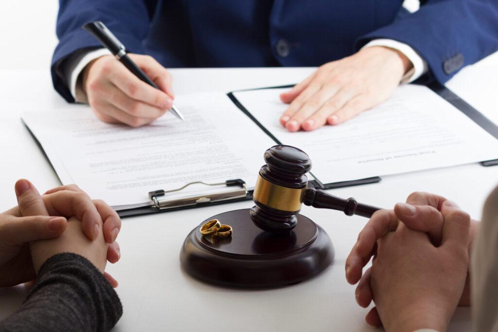 Divorce lawyer reviewing legal documents with a couple at a desk, with a judge&rsquo;s gavel and wedding rings symbolizing divorce or family law proceedings.
