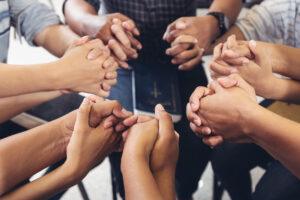 Group of people sitting in a circle with hands clasped in prayer around a Bible