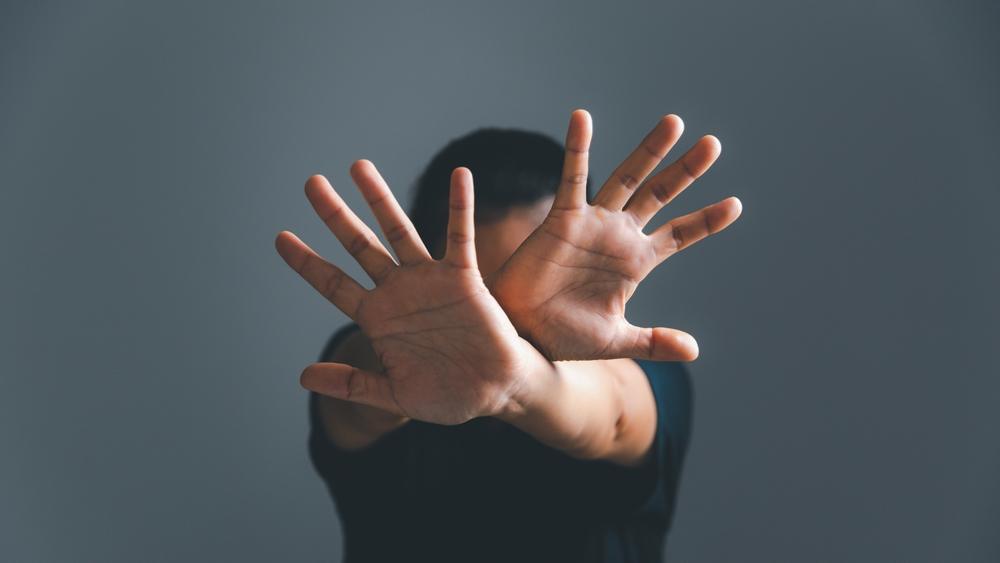 Person raising both hands in a defensive gesture to block or stop someone, symbolizing fear, personal protection, harassment, or abuse awareness.