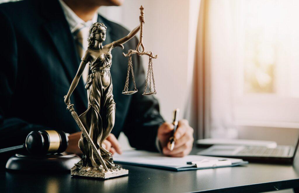 Statue of Lady Justice with lawyer writing at desk in office, symbolizing legal services and law practice