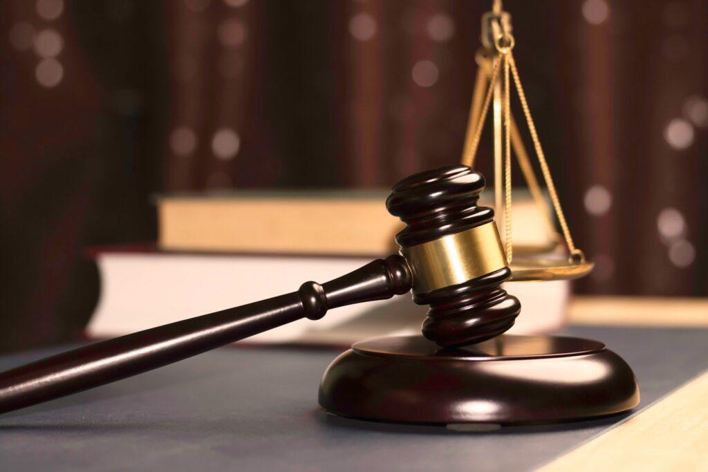 Judge&rsquo;s gavel and scales of justice on desk with law books in background, representing legal authority and courtroom justice