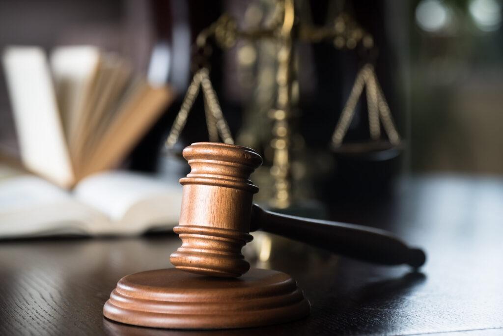 Wooden judge&rsquo;s gavel on a desk with law books and scales of justice in the background, symbolizing legal authority, courtroom decisions, and the justice system.