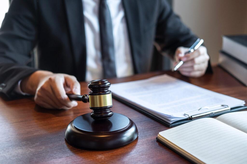 Lawyer holding a judge&rsquo;s gavel while reviewing legal documents at a desk, representing legal decision-making, court proceedings, or litigation services.