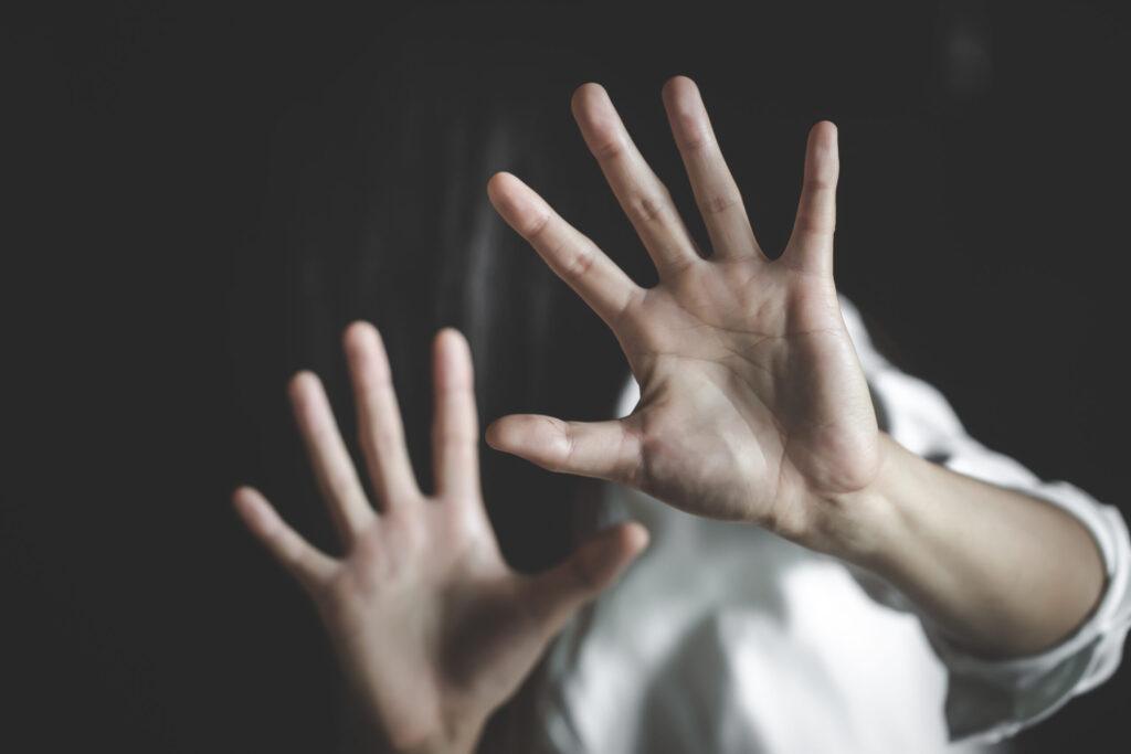 Woman raising both hands in a defensive gesture to protect herself, symbolizing fear, harassment, sexual assault, or domestic violence awareness.