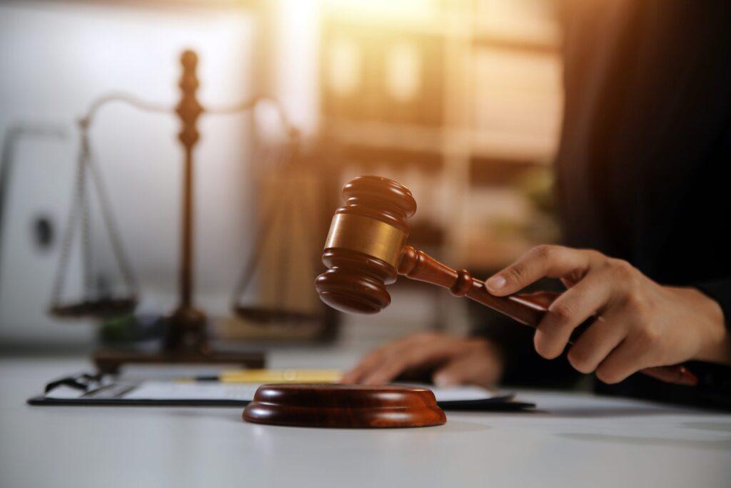 Judge holding a wooden gavel above the sound block with scales of justice in the background, symbolizing court rulings, legal authority, and the justice system.