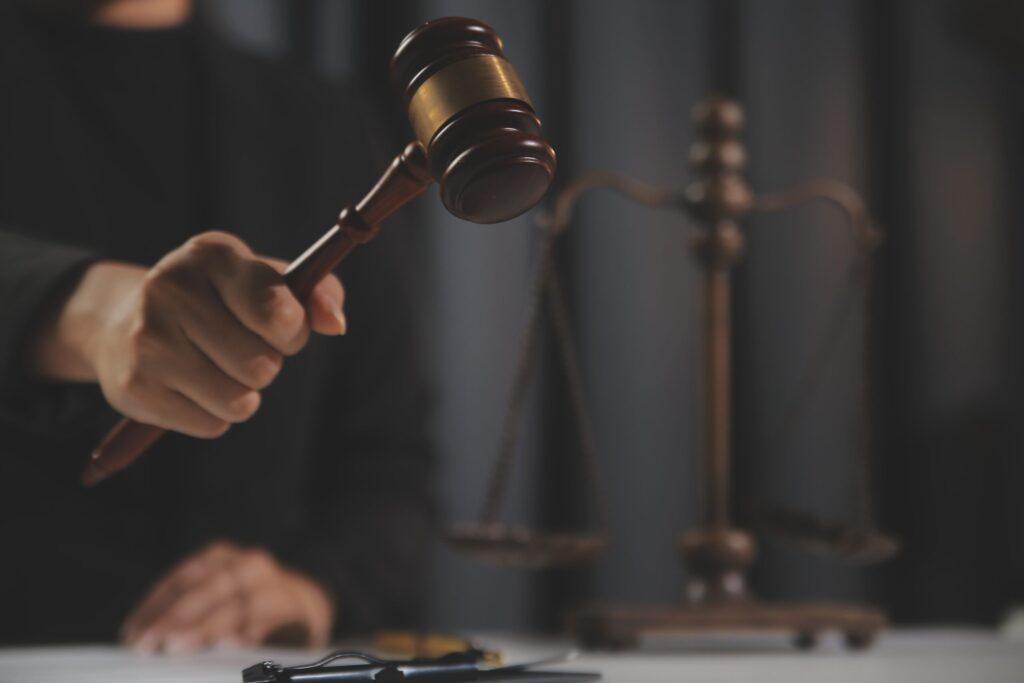 Judge holding gavel in courtroom with scales of justice in background