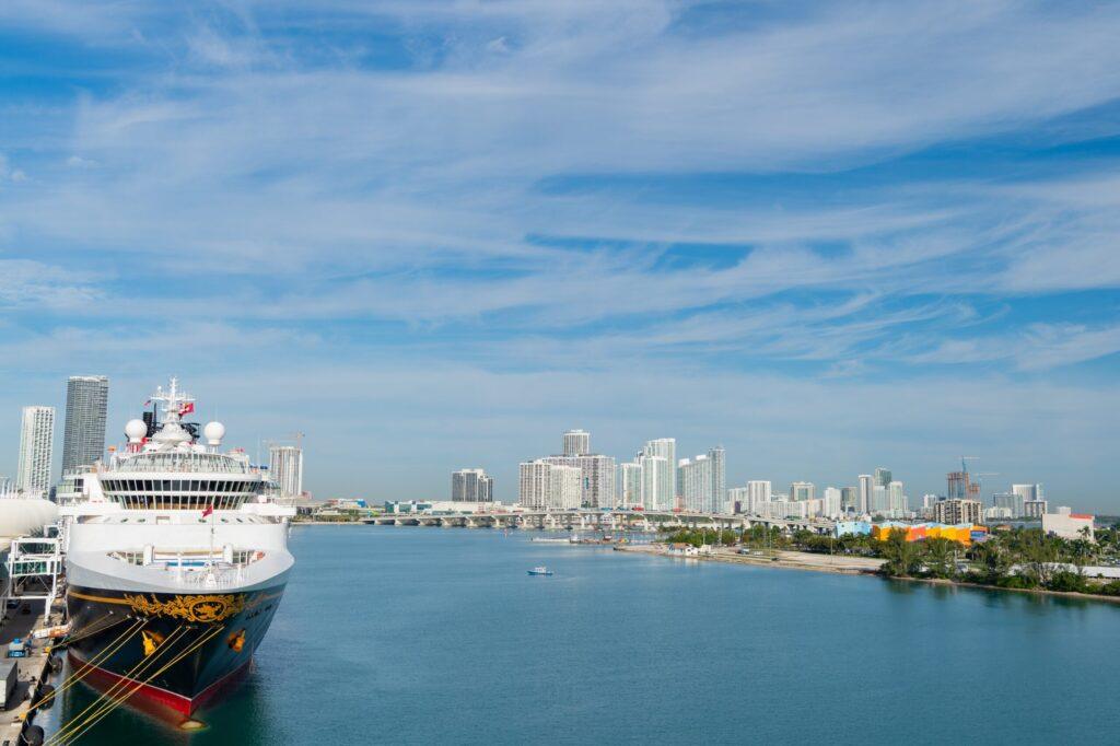Cruise ship docked in harbor with modern city skyline and waterfront in background under blue sky