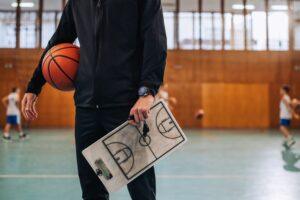 A  coach holding basket ball and clipboard with court drawing on it