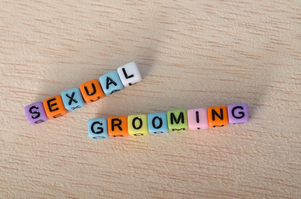 Colorful Letter Beads Spelling 'SEXUAL' and 'GROOMING' on Wooden Surface