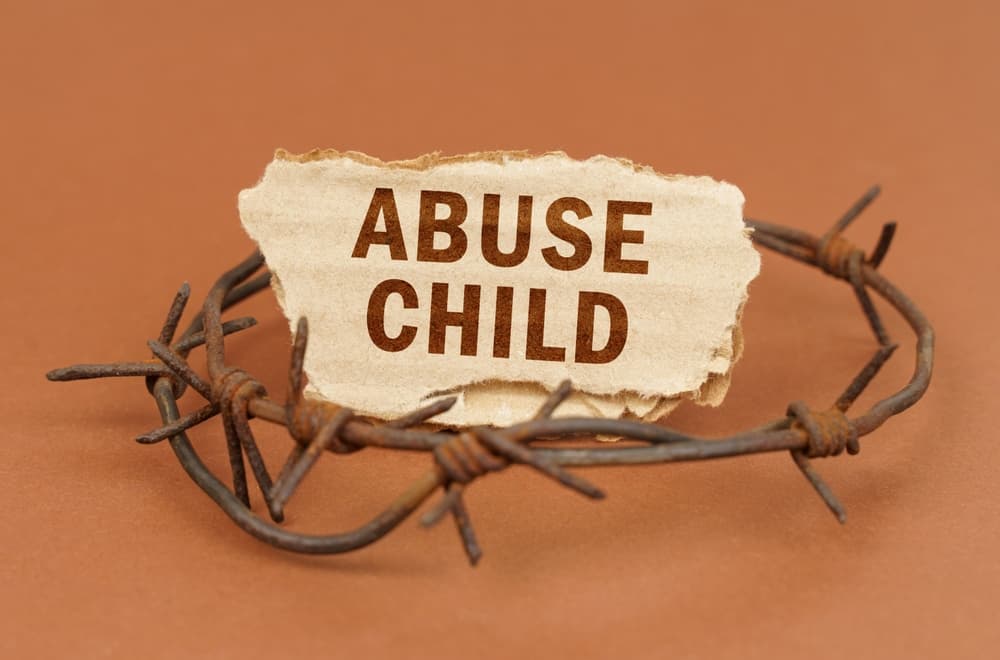 On a brown surface, barbed wire and a cardboard sign with the inscription - Child Abuse