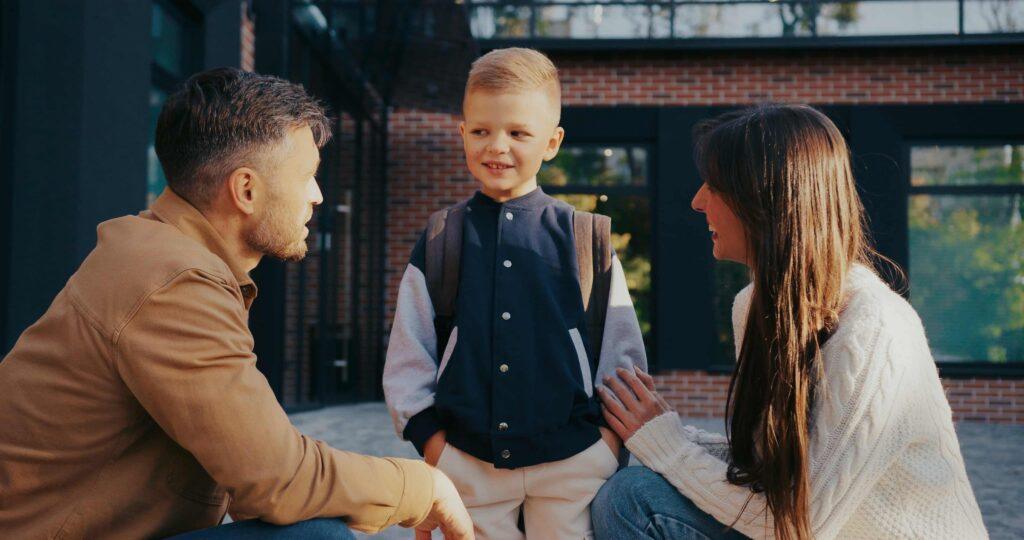 Divorced parents talking with their young son outside school during child custody exchange.