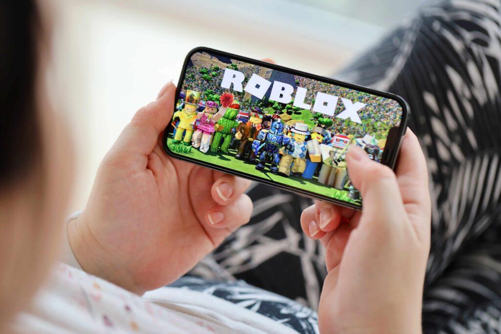 Person holding a smartphone and playing Roblox mobile game on the screen Person holding a smartphone and playing Roblox mobile game on the screen