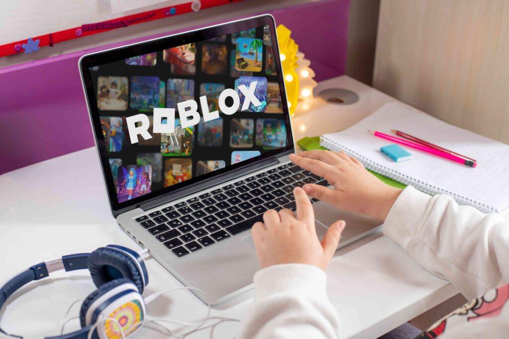 Child using a laptop to play Roblox at a desk with school supplies and headphones. Child using a laptop to play Roblox at a desk with school supplies and headphones.
