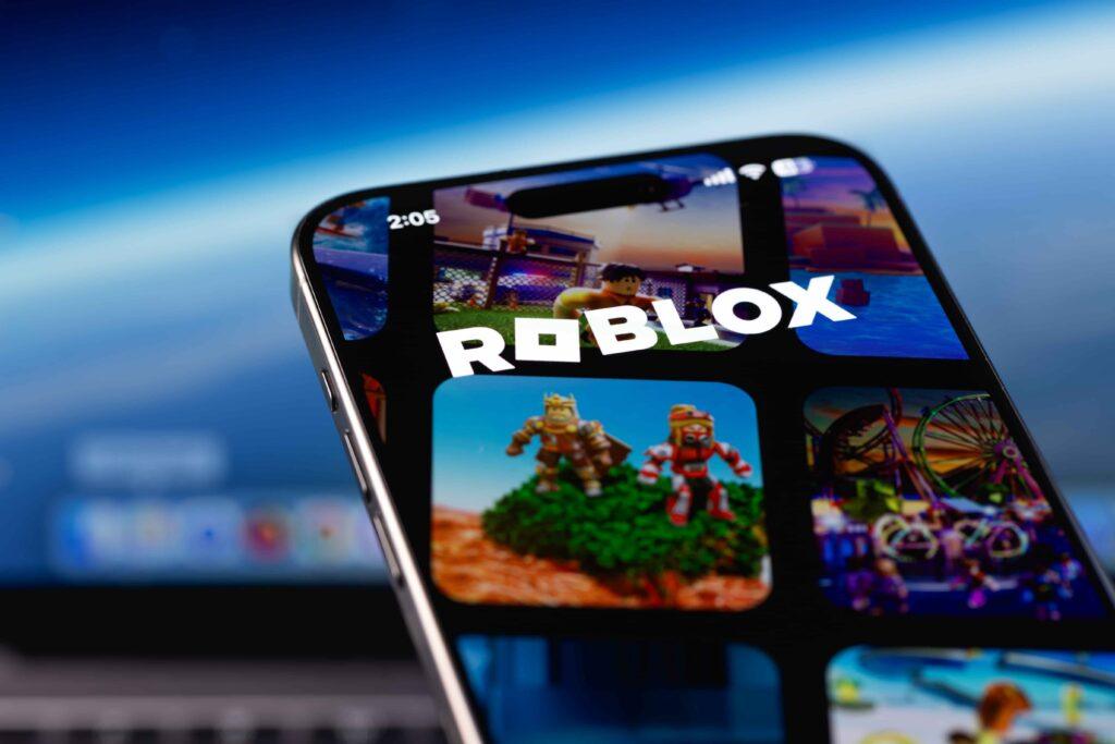 Close-up of smartphone screen displaying the Roblox app logo and game icons. Close-up of smartphone screen displaying the Roblox app logo and game icons.