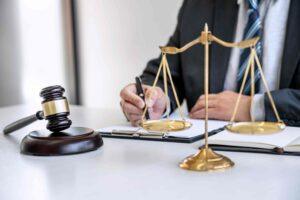 Lawyer writing notes at a desk with scales of justice and a judge’s gavel, representing legal consultation, justice, and professional law services.
