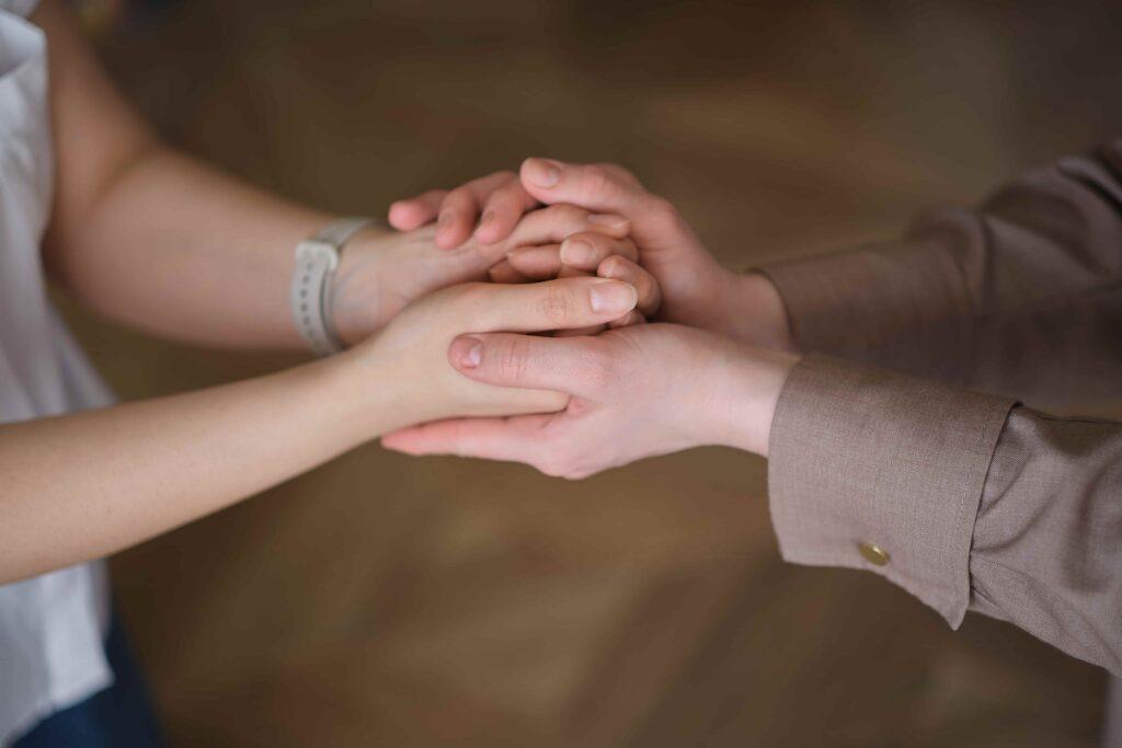 Close-up of two people holding hands in support, symbolizing emotional comfort, compassion, and assistance for someone in distress.