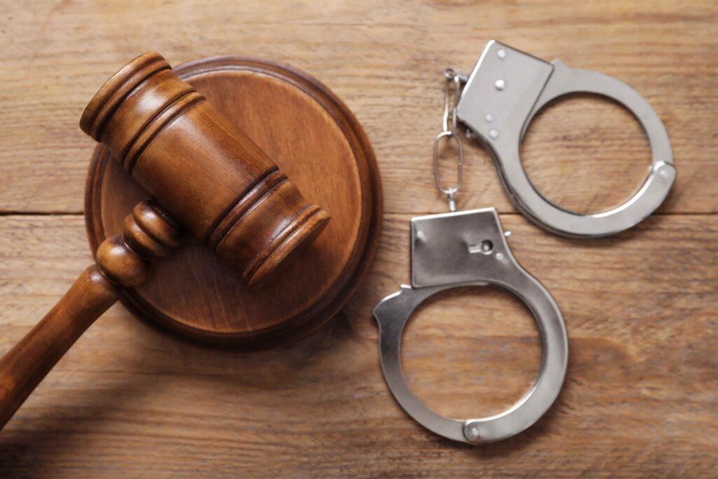 Judge&rsquo;s gavel and metal handcuffs on a wooden table, symbolizing criminal law, arrest, legal consequences, and the justice system.