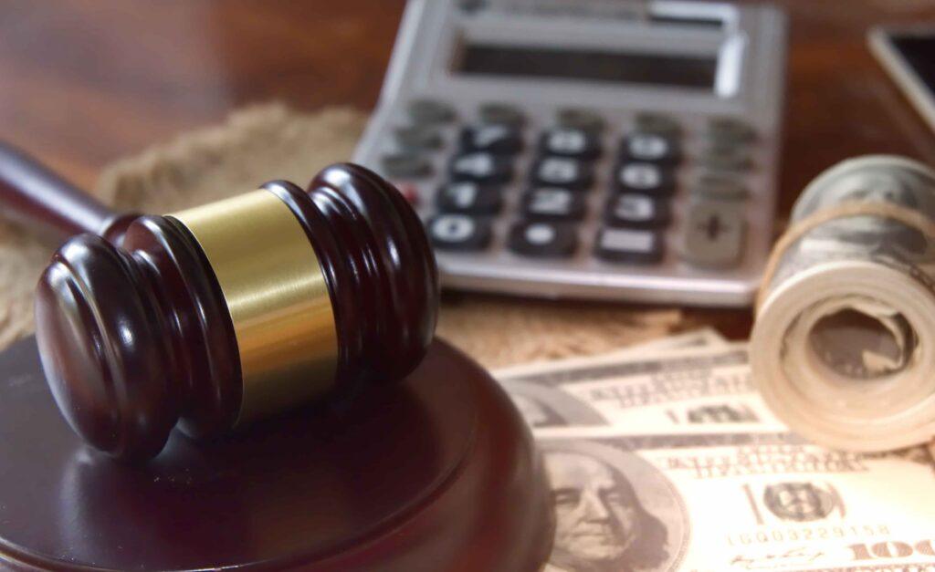 Judge&rsquo;s gavel on desk with cash and calculator in background, representing legal financial matters or settlement costs