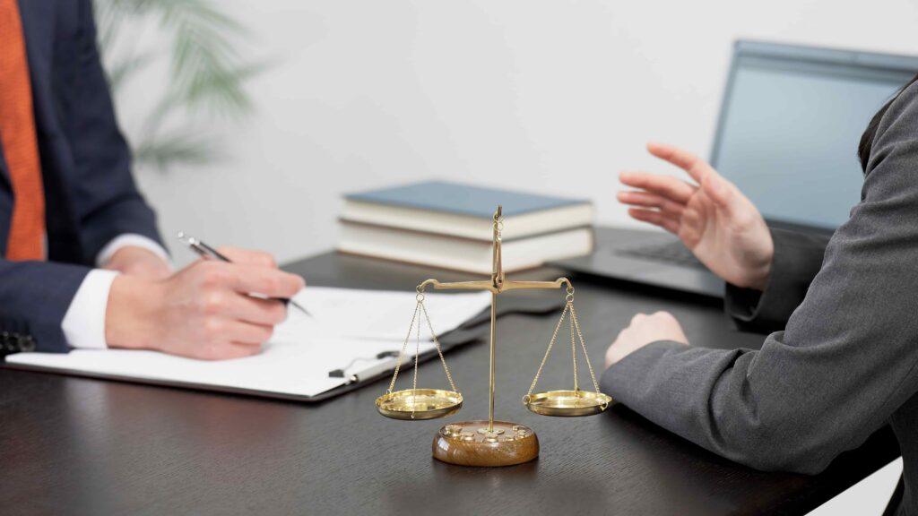 Lawyer consulting with a client at a desk with scales of justice, discussing legal case details during a professional legal consultation.