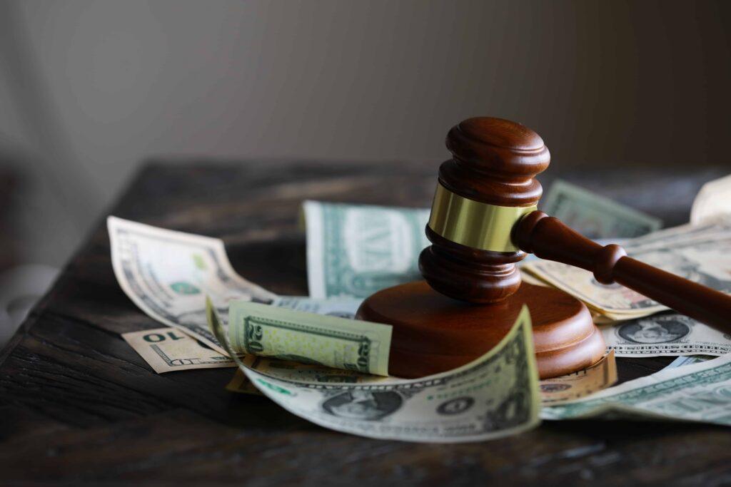 Judge&rsquo;s gavel resting on US dollar bills, symbolizing legal costs, financial penalties, or lawsuit settlements
