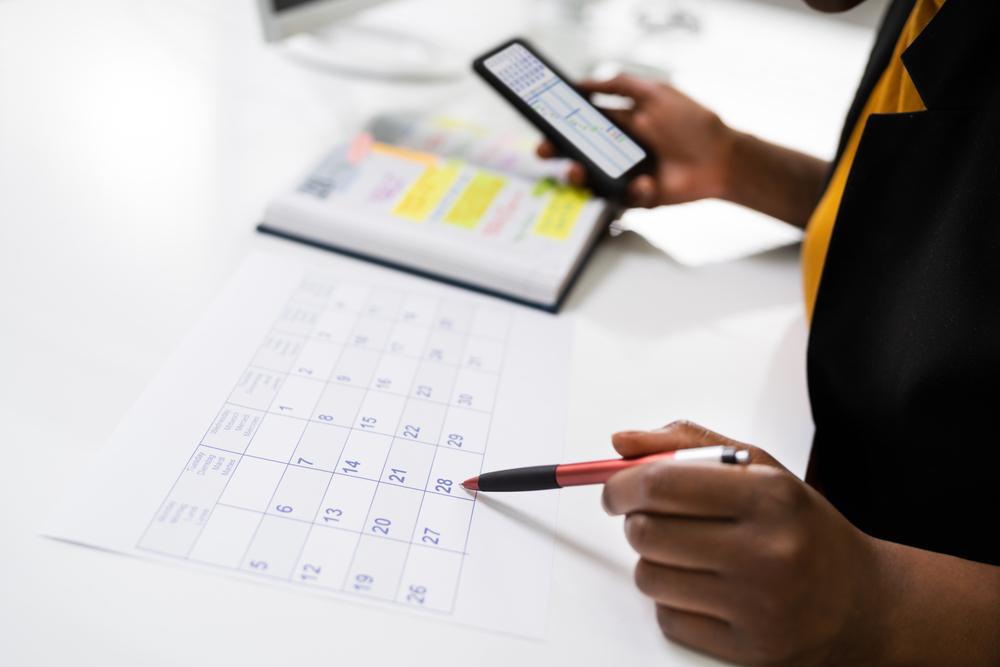 Over-the-shoulder image of person tracking deadlines on calendar and phone